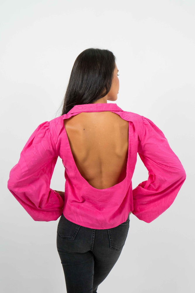 Pink shirt with a wide rounded bare back. Slightly puffed long sleeves. It has a textured cotton fabric.