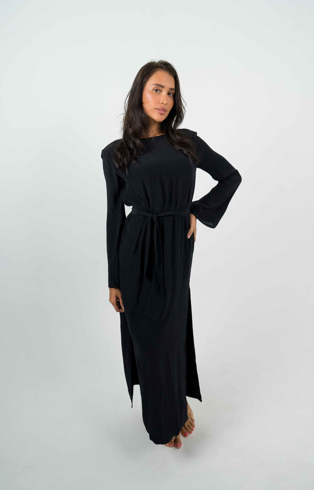 
            
                Load image into Gallery viewer, Long black backless dress with long sleeves. Can be belted at the waist and is open on the left side.
            
        