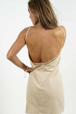 Beautiful bare back of a short dress in beige linen. It has details all over the front of it.