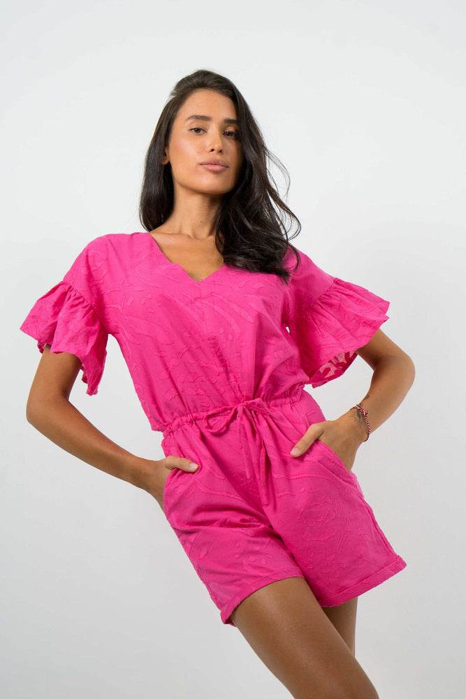 model is wearing cute pink playsuit with puff sleeves and adjustable waist lace. By Back Cartel