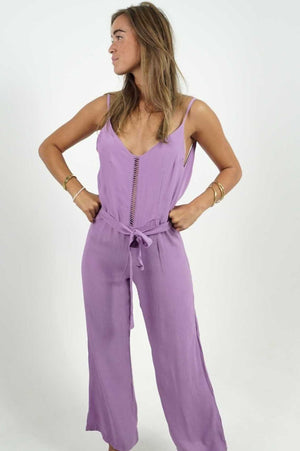 Backless purple jumpsuit with a straight cut. The lower legs are flared, in a fluid and light material. Adjustable belt.