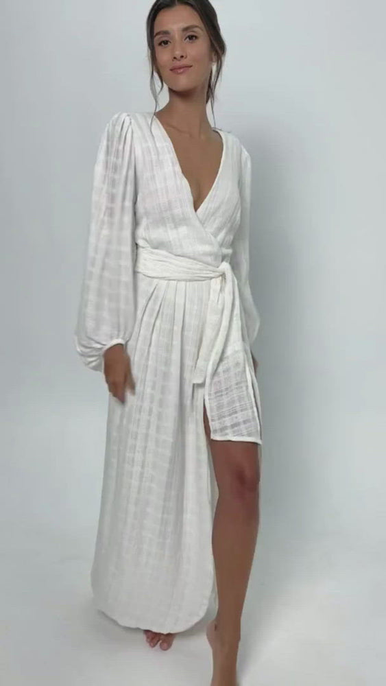 
            
                Load and play video in Gallery viewer, Short video of a young woman wearing a long white cotton wrap backless dress. With puff sleeves and a V-neckline.
            
        